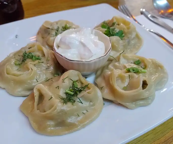 Manty na talerzu, obok miseczka śmietany